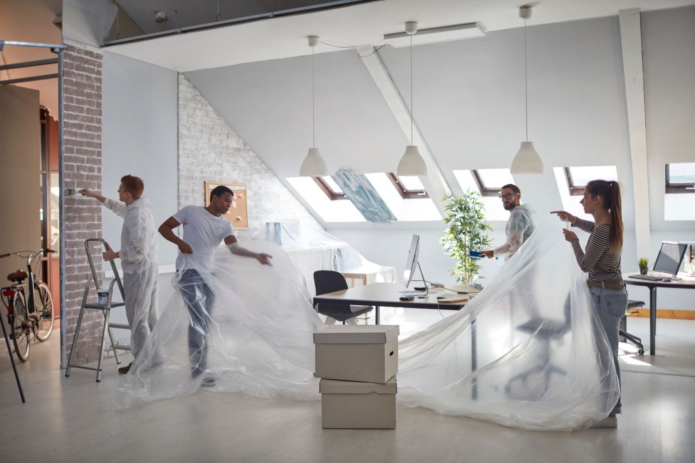 Four people covering furniture with drop sheets as they start painting a room.